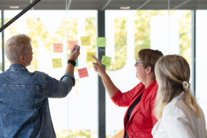 teamfoto met postits voor een glazen wand in een kantoor